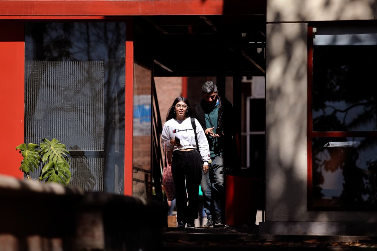 Dos estudiantes salen por el acceso de un edificio con marcos rojos.