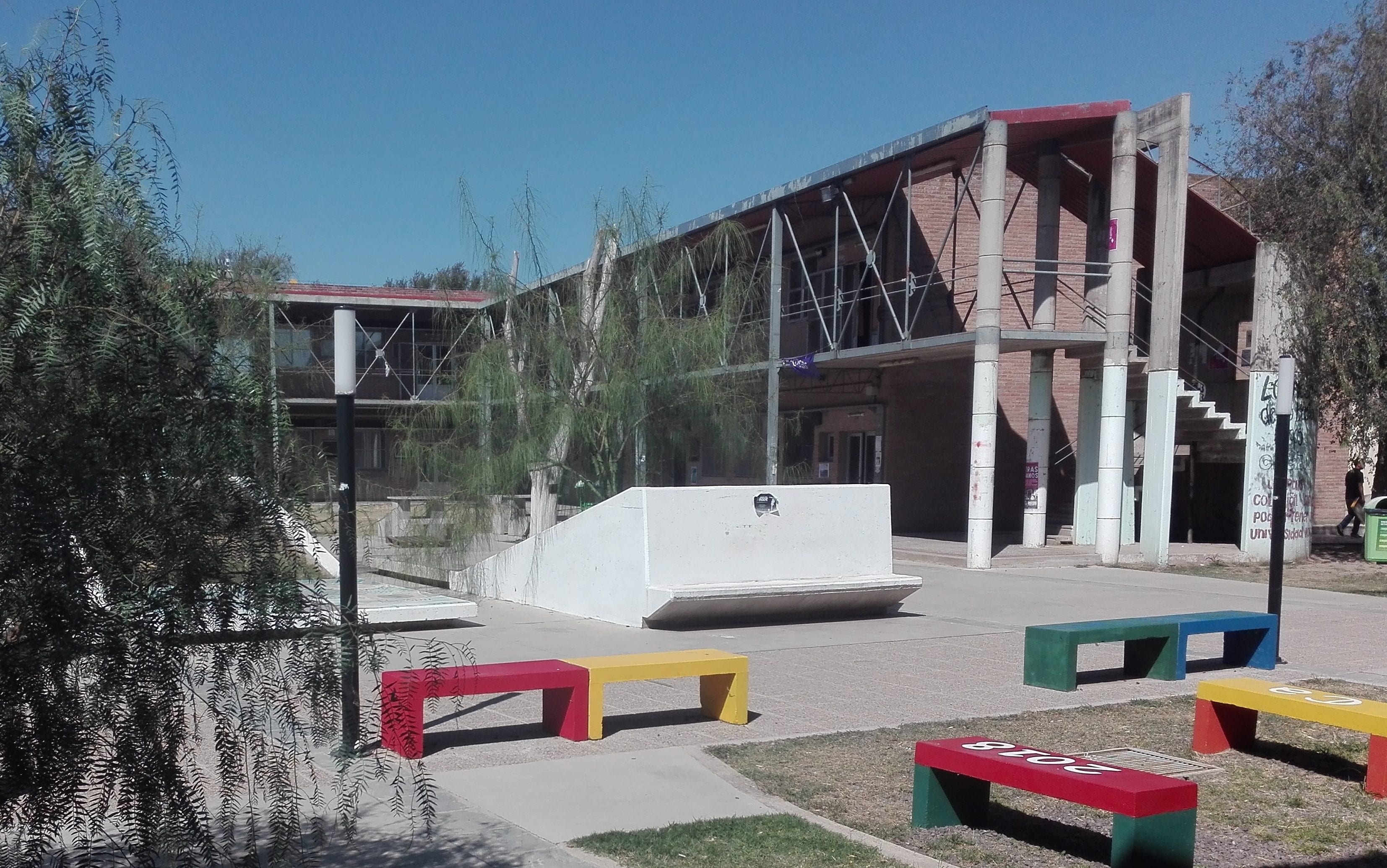 Edificio del campus de la Universidad Nacional de Río Cuarto con patio y bancos de colores.