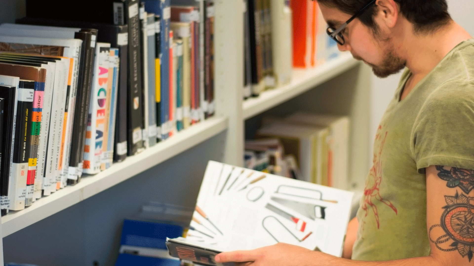 Persona consultando un libro junto a estanterías de biblioteca