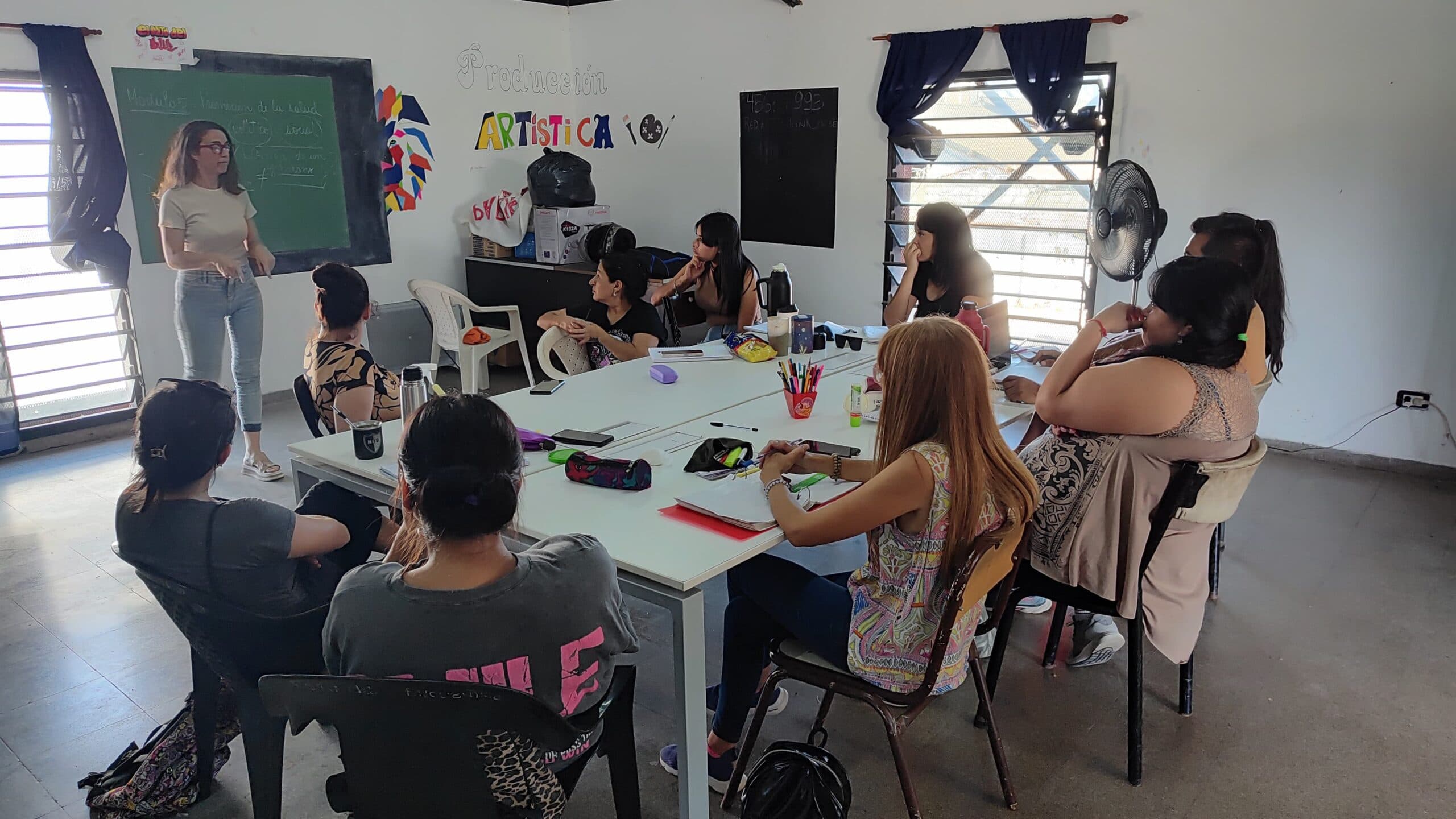 Grupo de estudiantes reunido alrededor de una mesa en un aula, con materiales de trabajo.