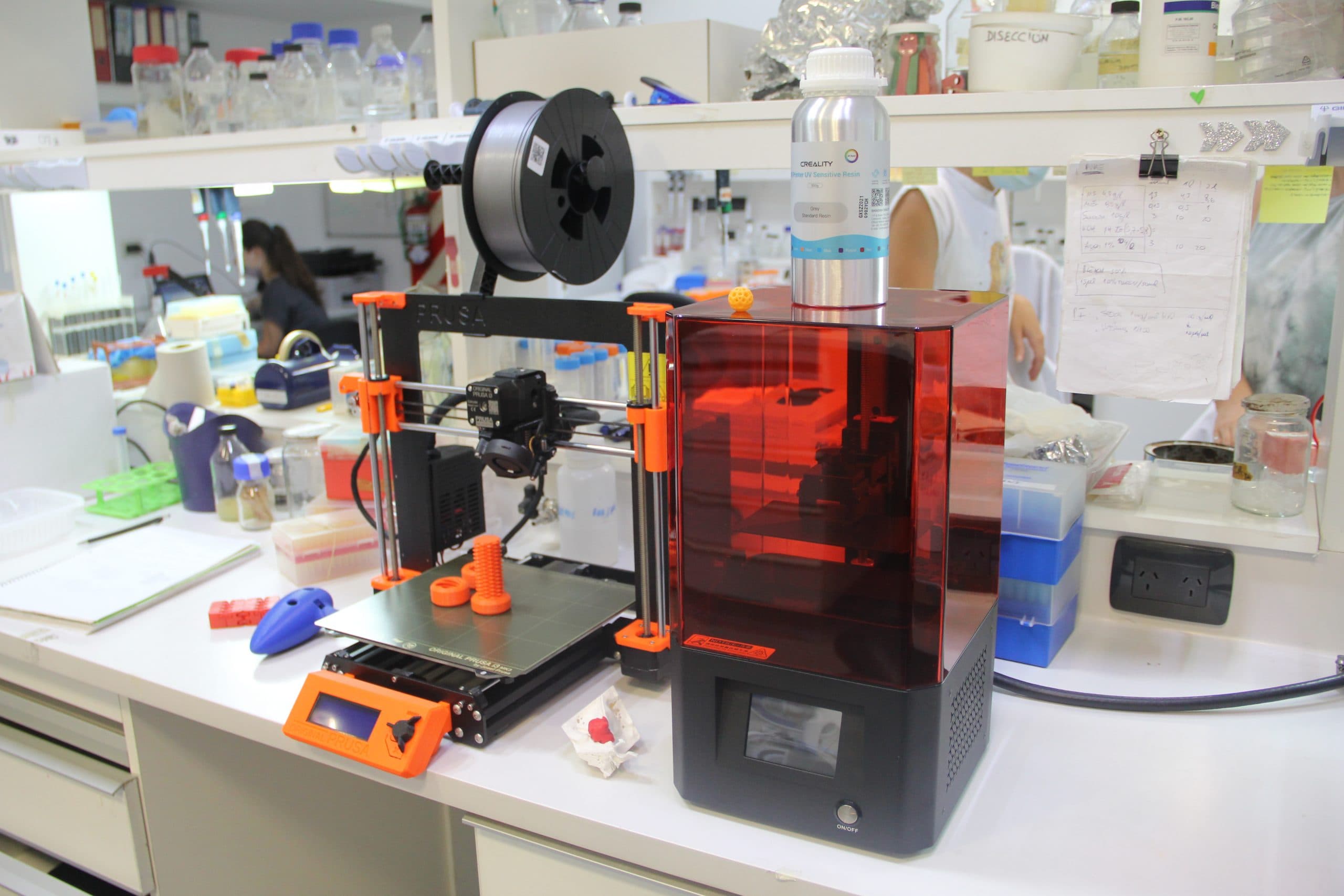 Impresoras 3D y materiales de trabajo sobre una mesa de laboratorio.