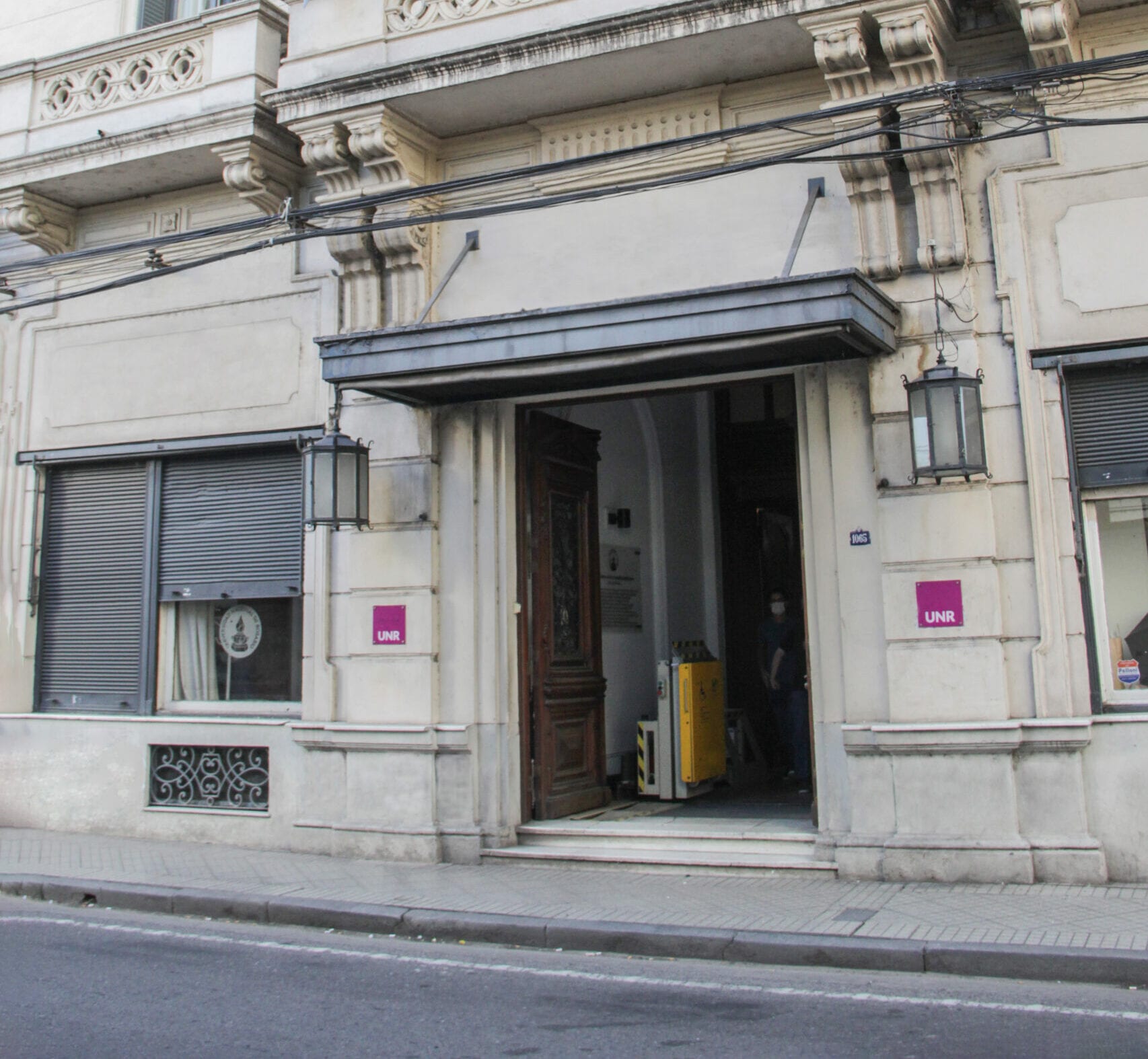 Fachada de una sede de la Universidad Nacional de Rosario, con ingreso sobre la vereda y señalética institucional.