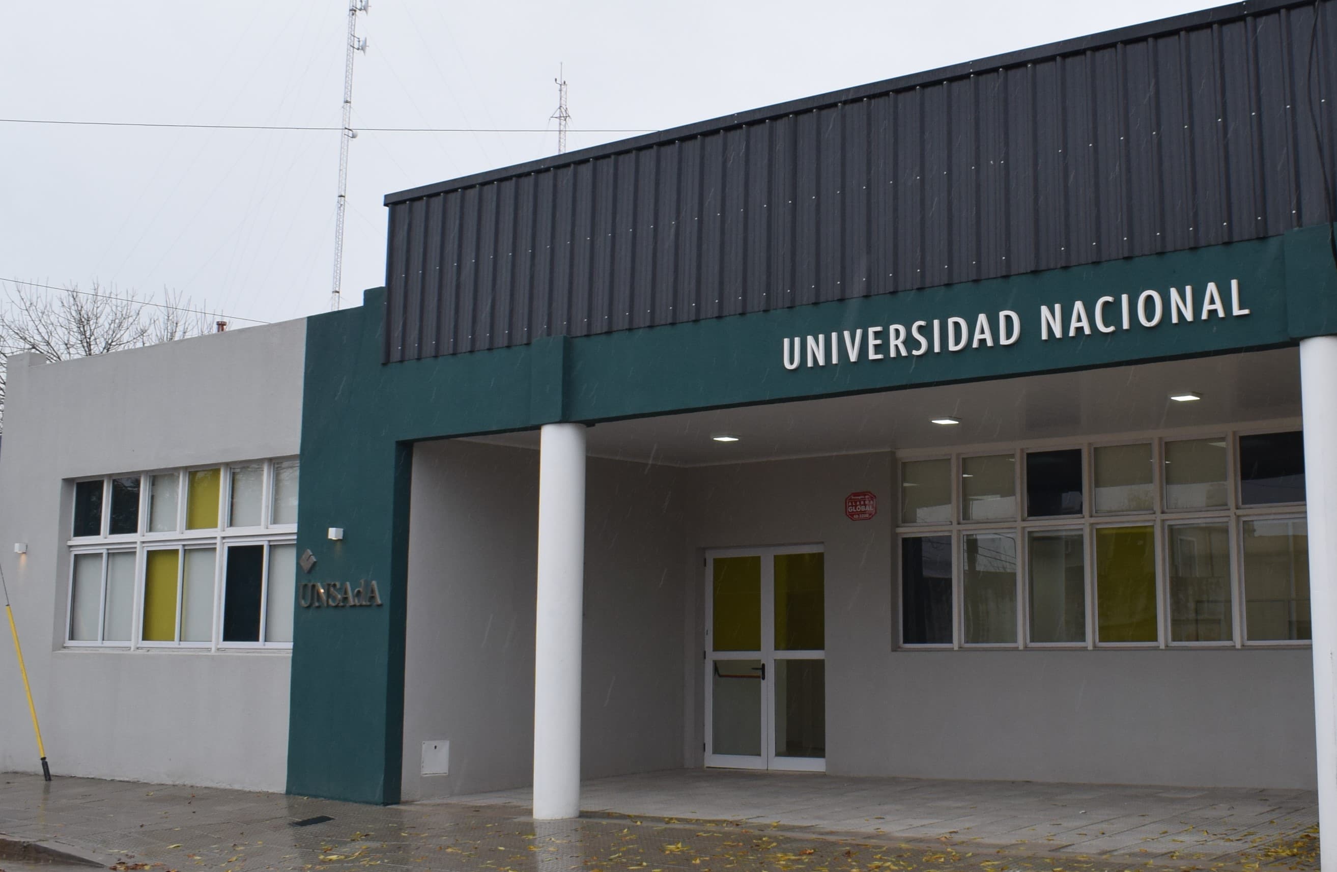 Frente de una sede universitaria con el nombre Universidad Nacional sobre la entrada.