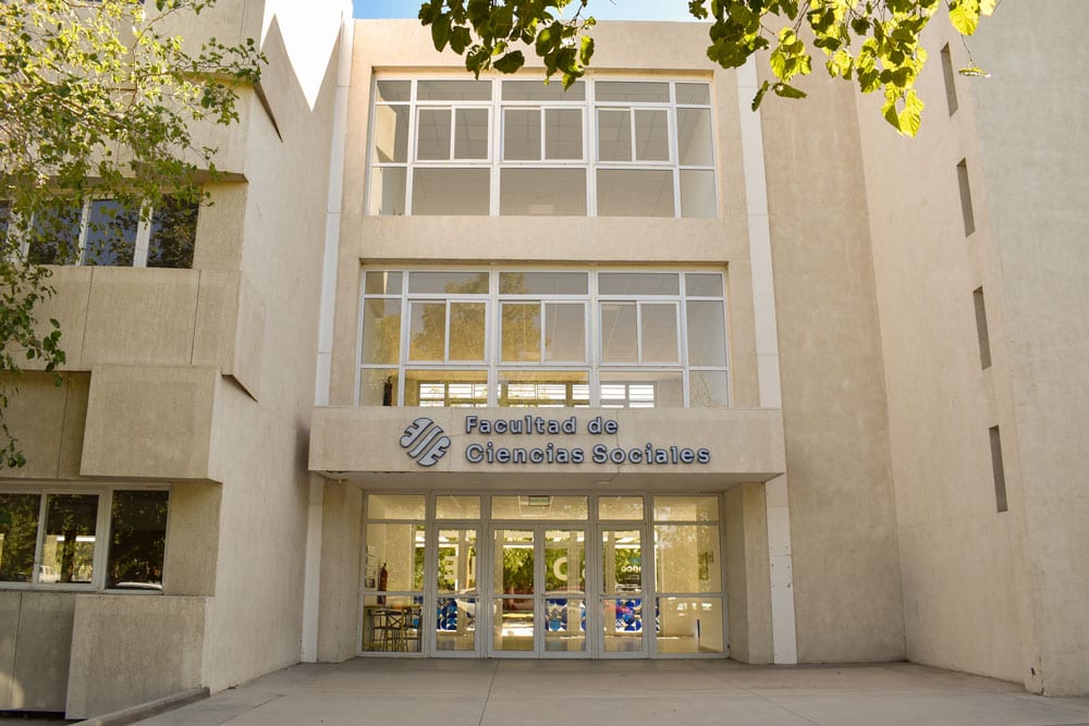 Fachada de la Facultad de Ciencias Sociales con acceso vidriado y cartelería institucional