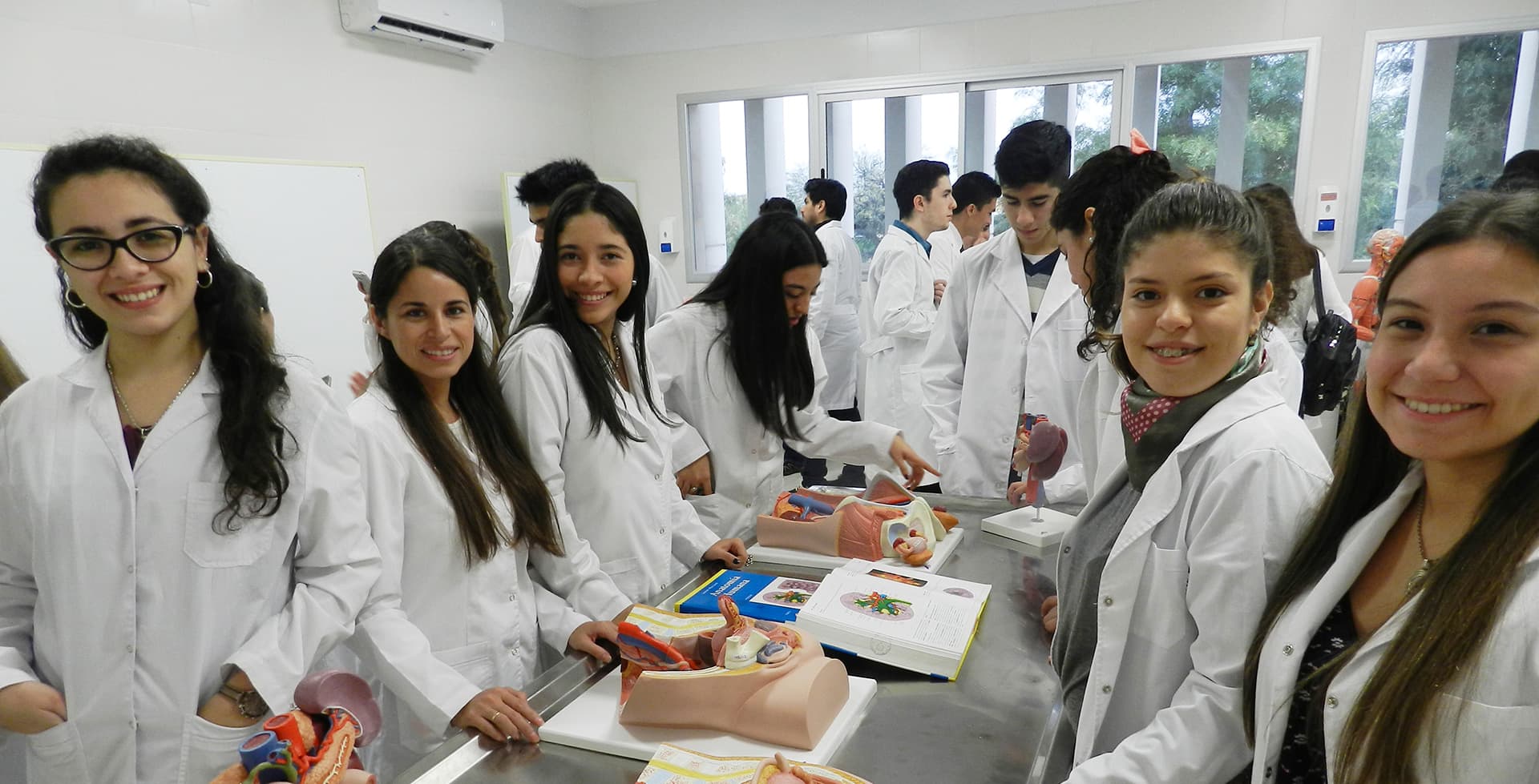 Estudiantes con guardapolvos reunidos alrededor de materiales de estudio en un laboratorio.