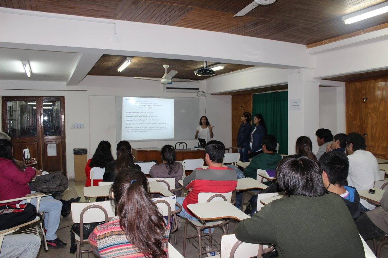 Estudiantes sentados en un aula durante una exposición con proyector.