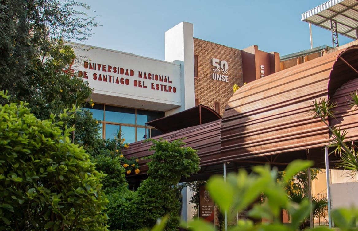 Fachada de la Universidad Nacional de Santiago del Estero, vista entre árboles y vegetación.