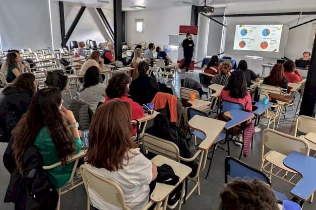 Estudiantes sentados en un aula mientras una persona expone frente a una pantalla de proyección.