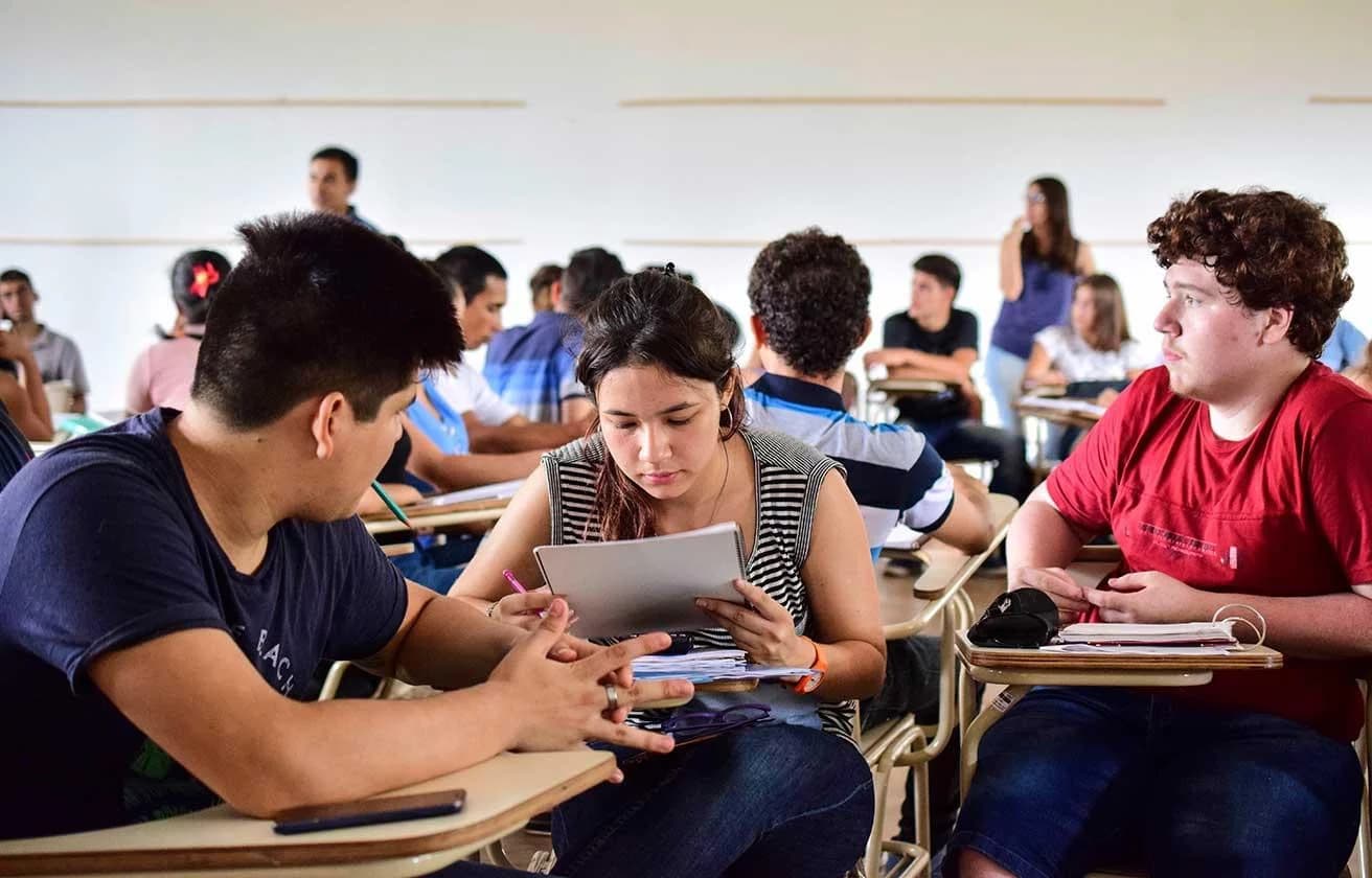 Estudiantes trabajan en grupo en un aula con pupitres