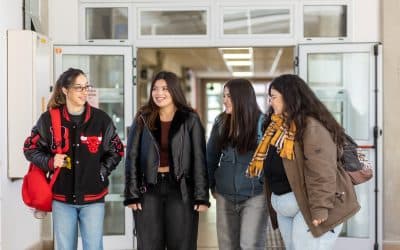 Cuatro estudiantes conversan frente a la entrada de un edificio universitario.
