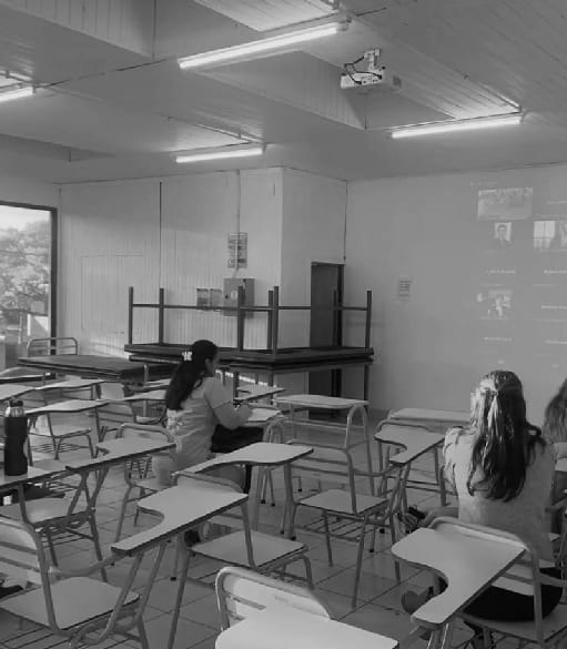 Aula con pupitres, estudiantes y una proyección en pantalla.