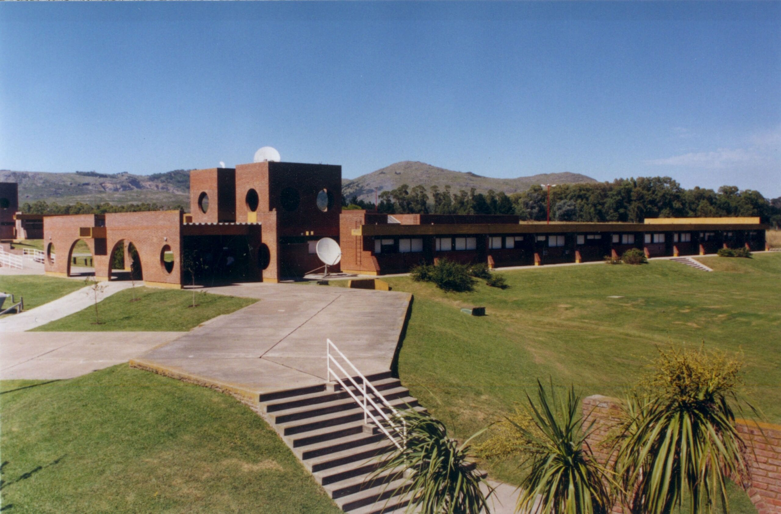 Vista amplia de un edificio de ladrillo, senderos y áreas verdes del campus universitario