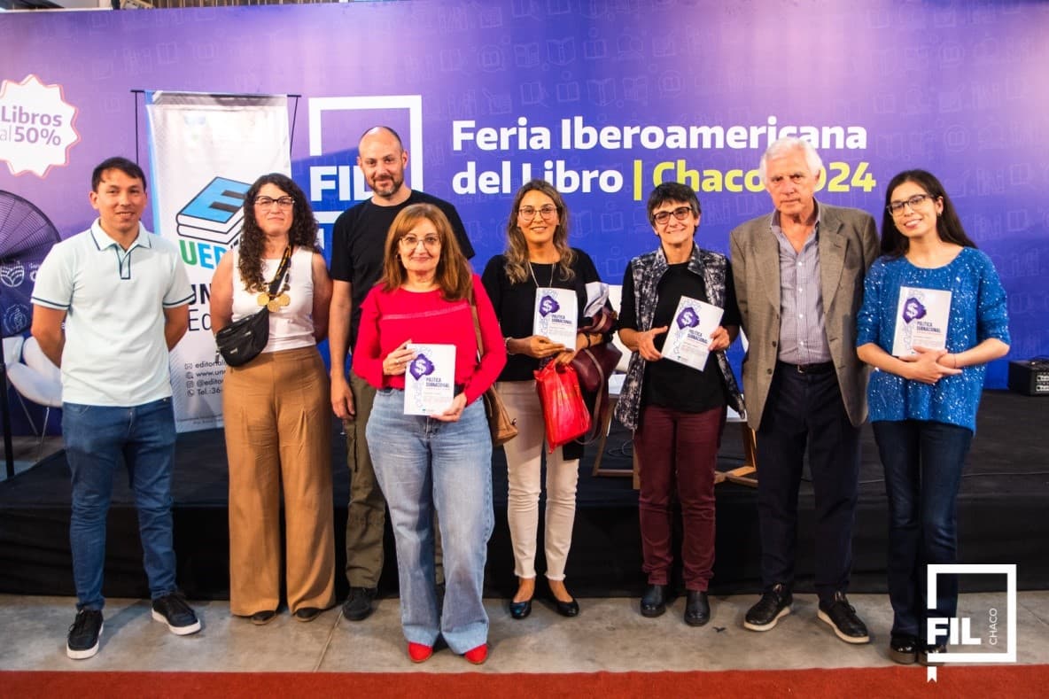 Grupo de participantes junto a un estand de la Editorial UNCAUS en una feria del libro.