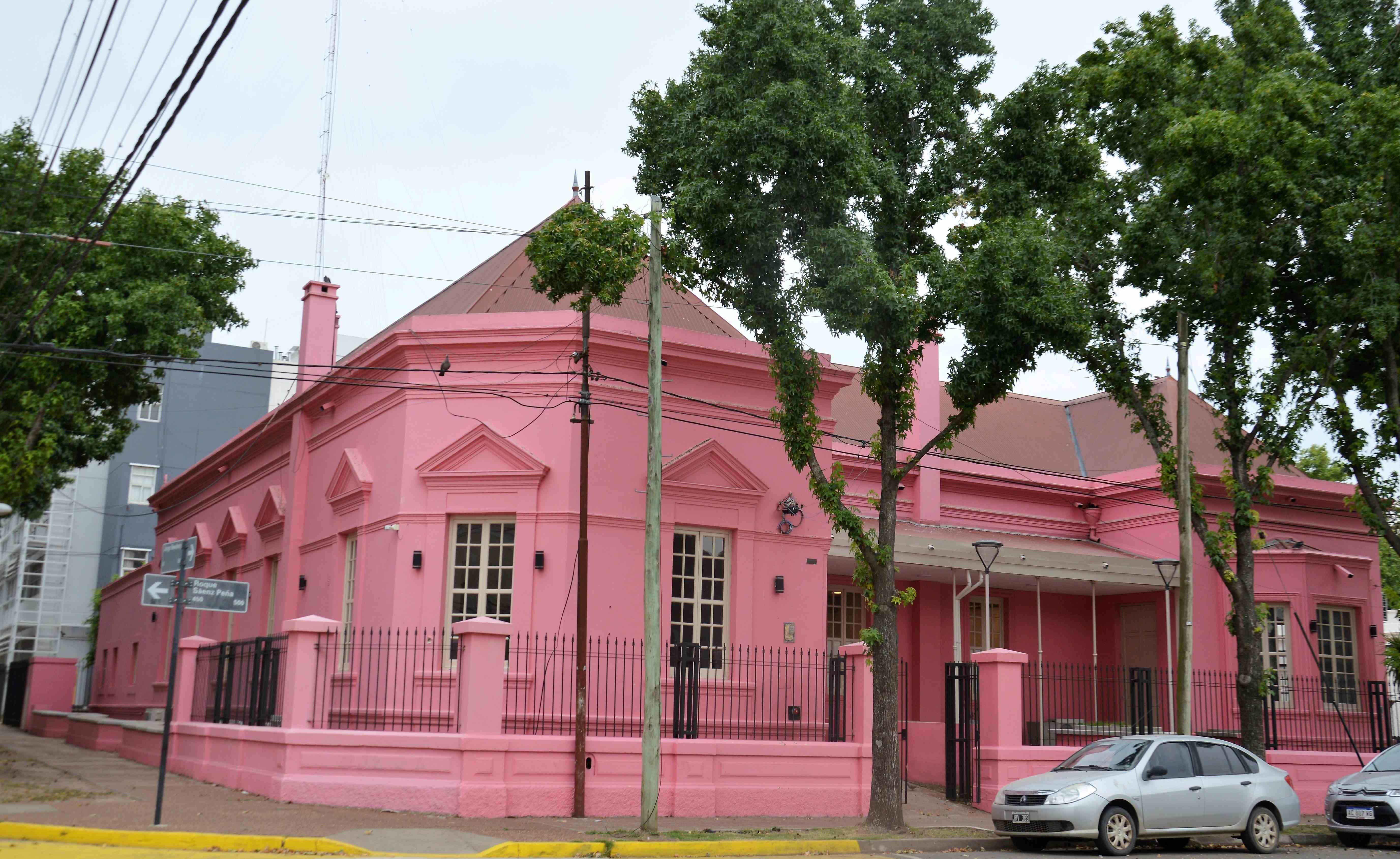 Fachada rosa de un edificio universitario vista desde la calle, con árboles en la vereda.