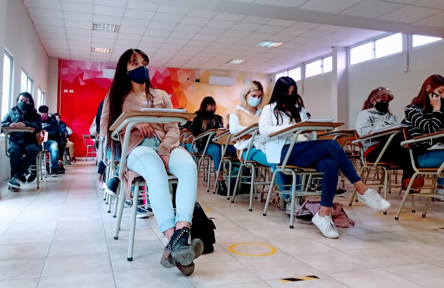 Estudiantes sentados en un aula, con cuadernos y escritorios individuales.