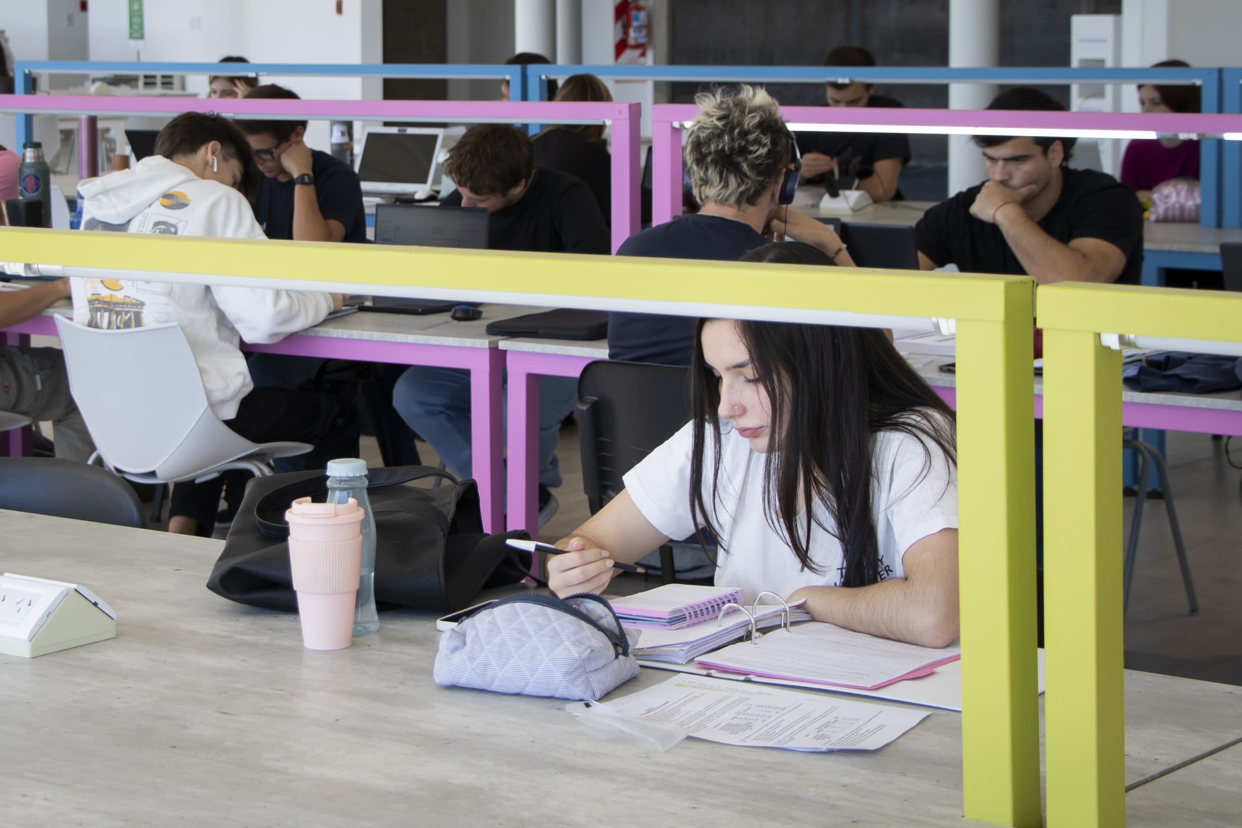 Estudiantes estudian en mesas de una sala de lectura con divisores de colores.