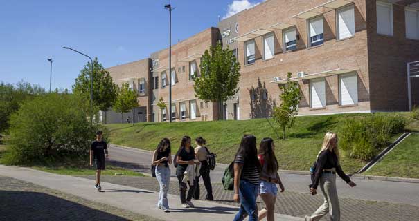 Estudiantes caminan por un sendero frente a un edificio de ladrillo del Campus Palihue.