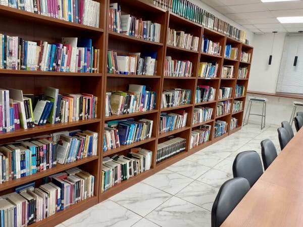 Estanterías con libros y mesa de lectura en la biblioteca de la UNPAZ.