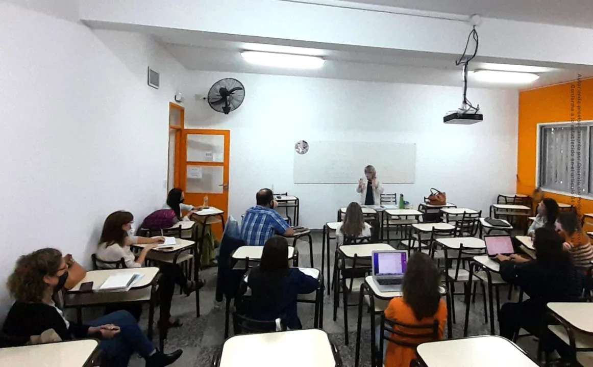 Aula con estudiantes sentados frente a una docente durante una clase.
