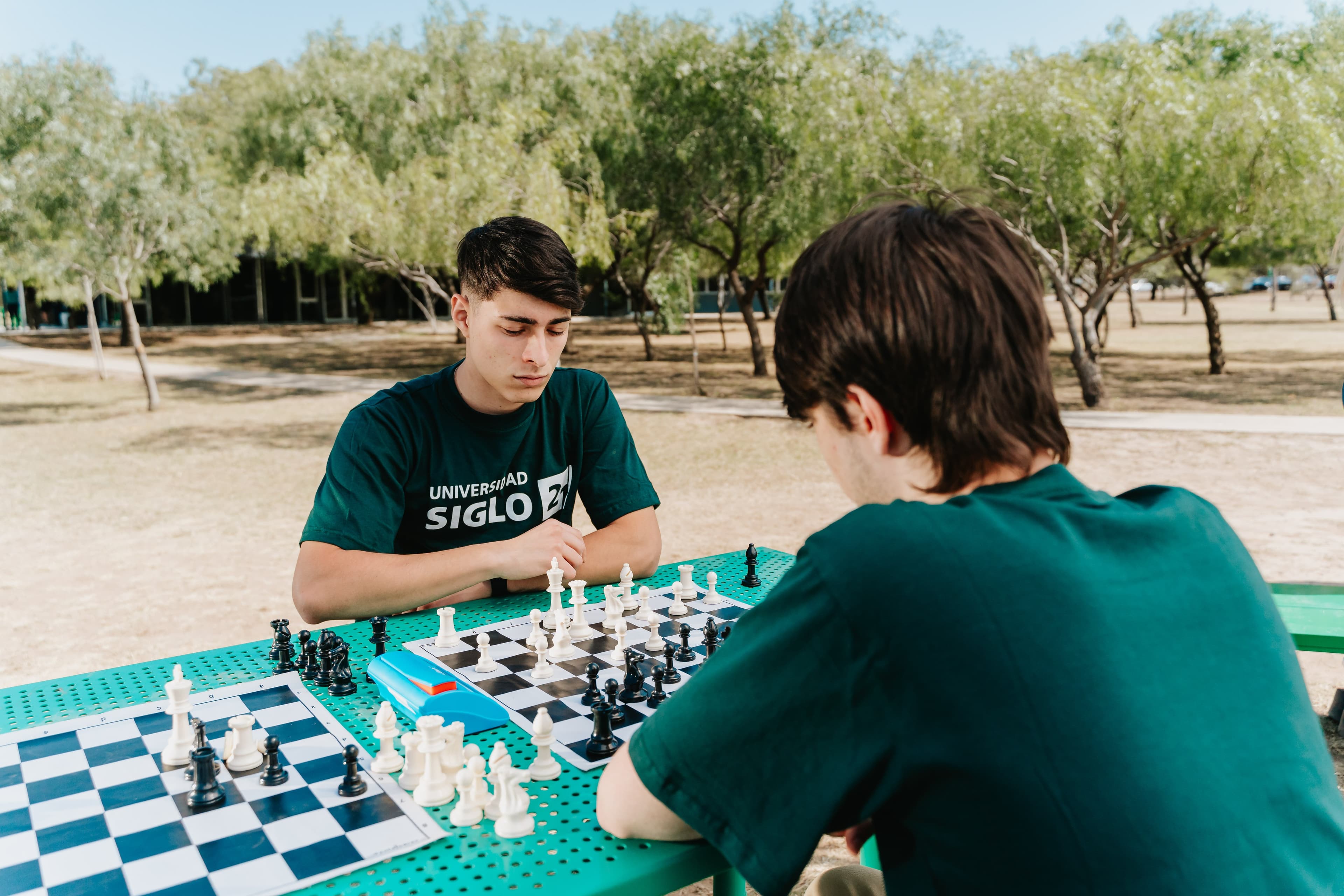 Dos estudiantes juegan ajedrez en una mesa al aire libre.