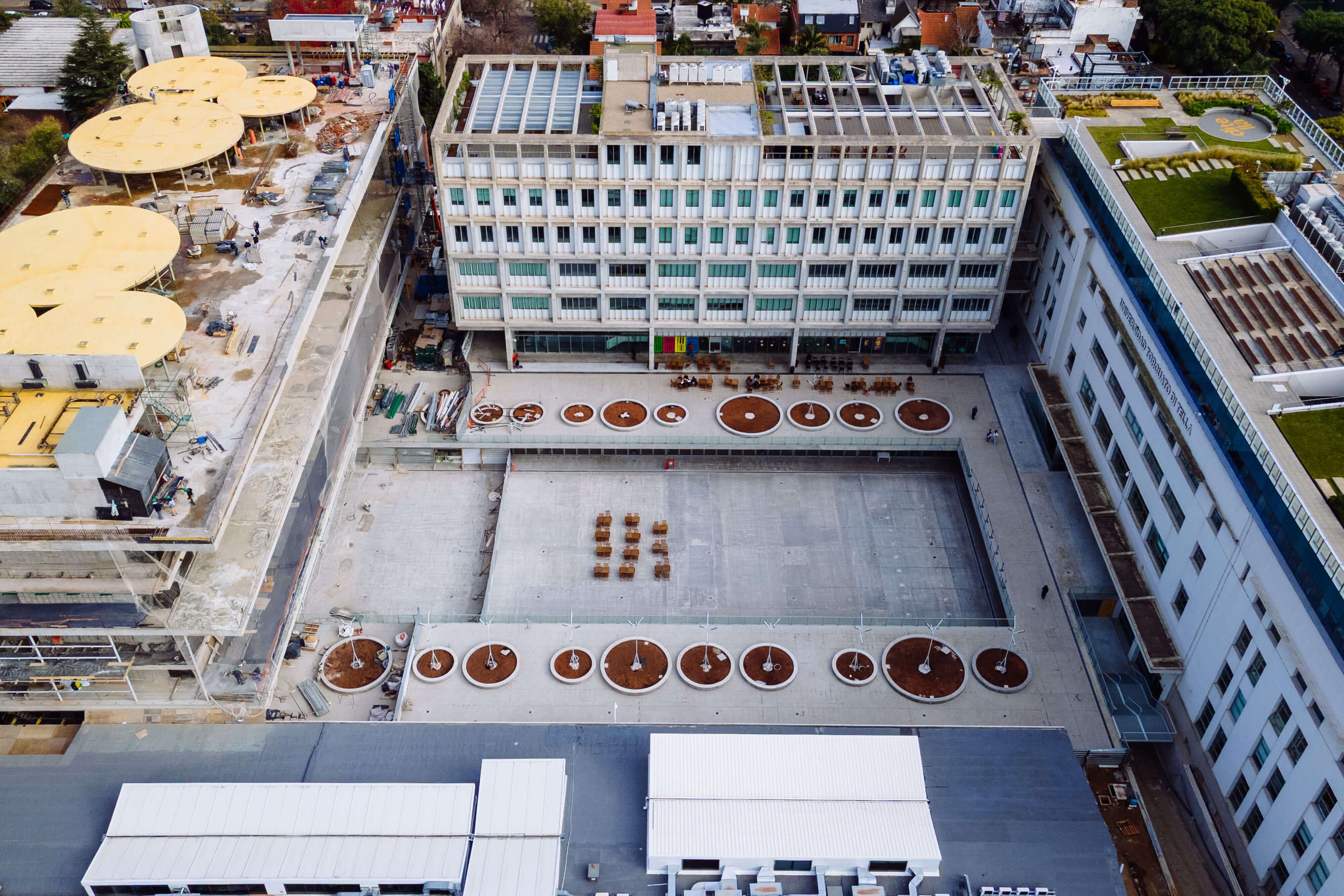 Patio interior del campus con edificios de varias plantas y mesas circulares.