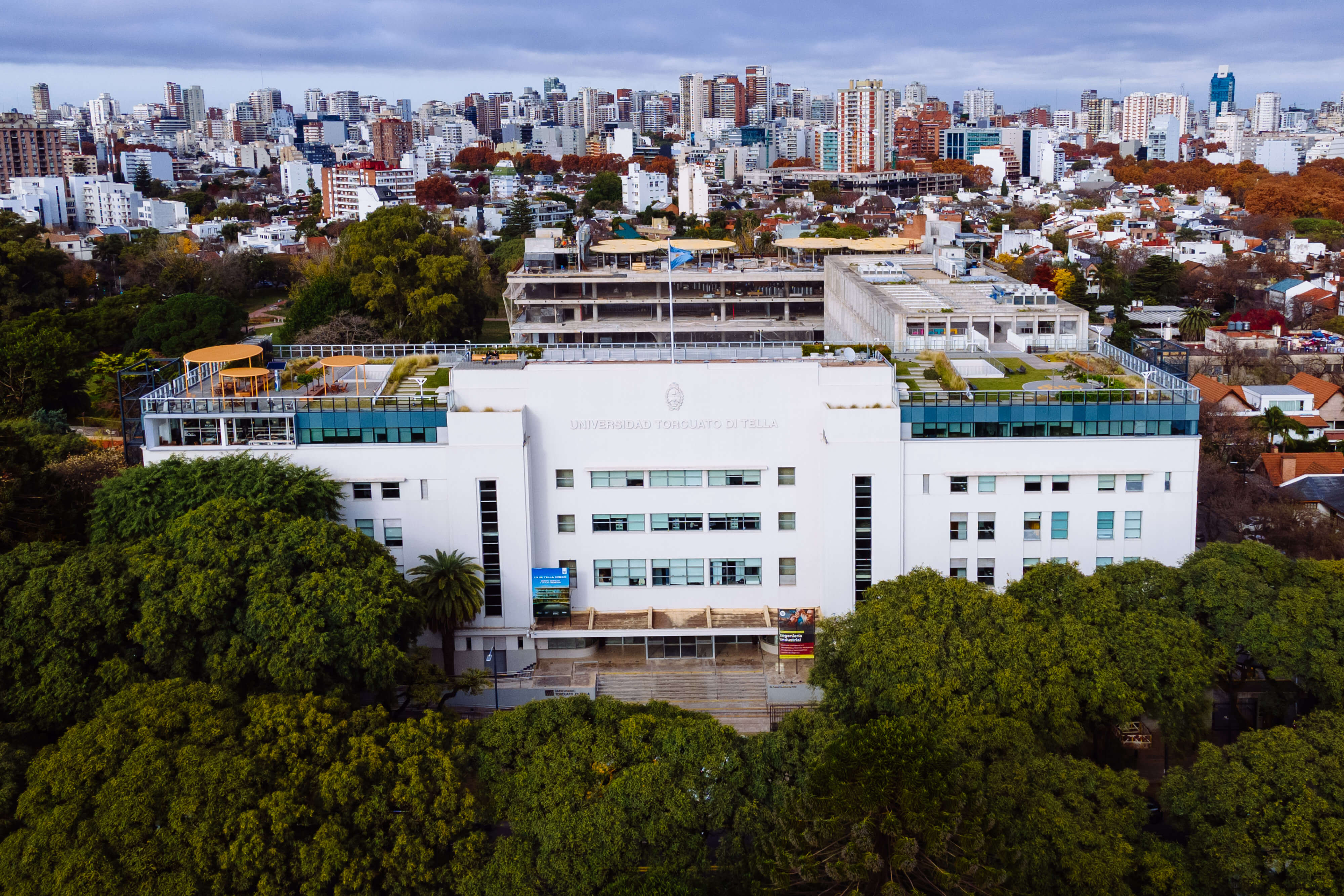 Vista aérea de edificios del Campus Di Tella rodeados de arbolado y ciudad.